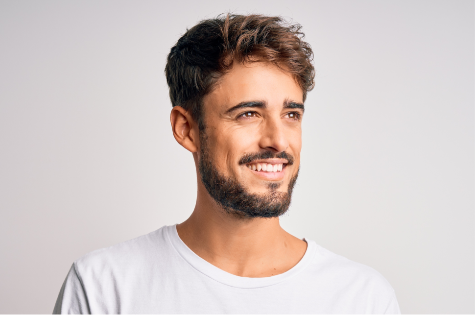 Young handsome man with beard wearing casual t shirt standing over white background looking away to side with smile on fac